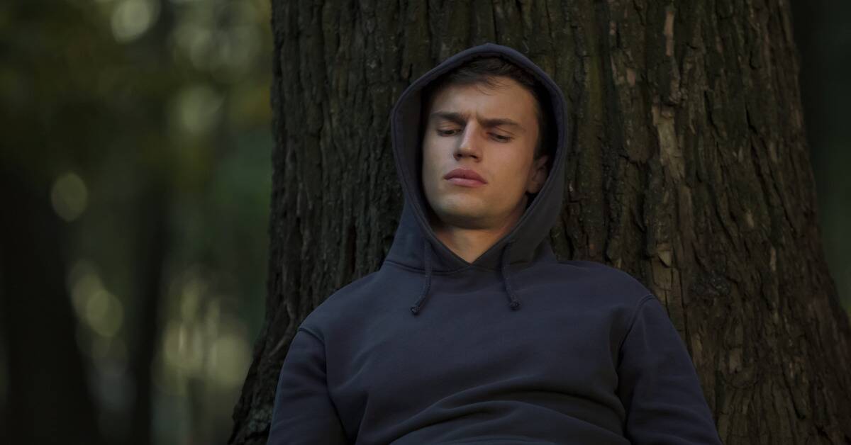 A man leaning against a tree, looking down on himself.