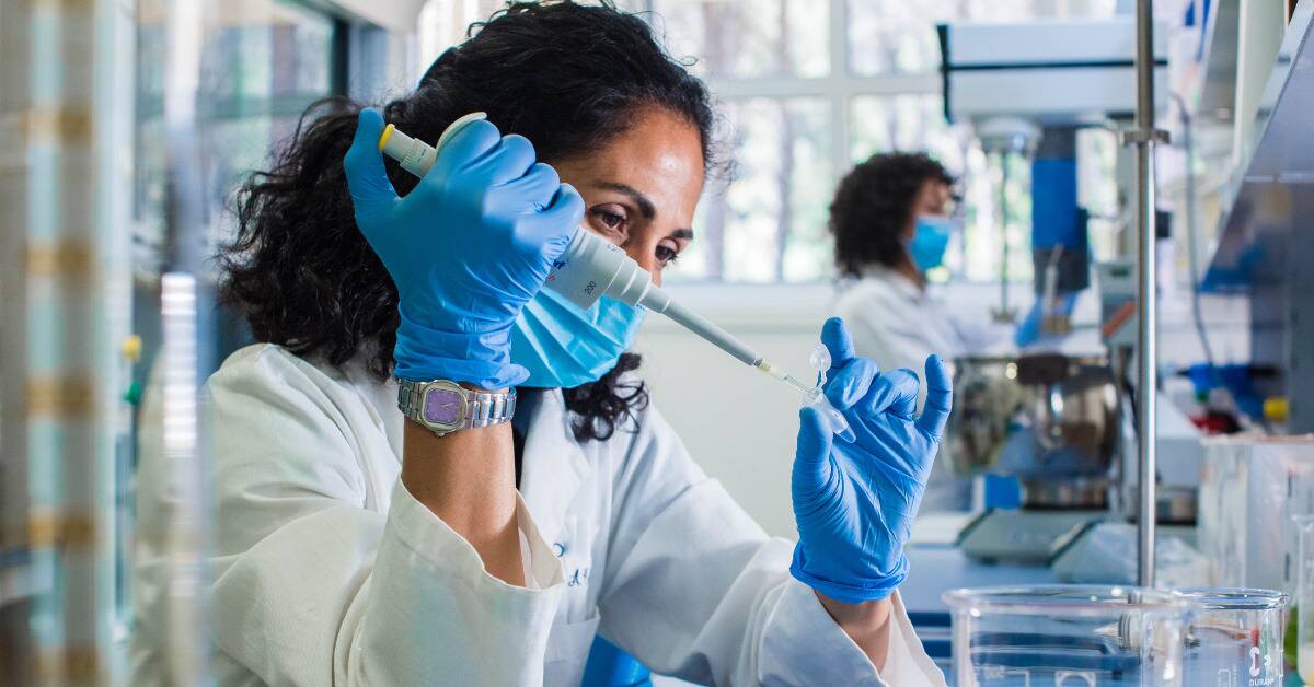 A woman working in a science lab, injecting something into a small container.