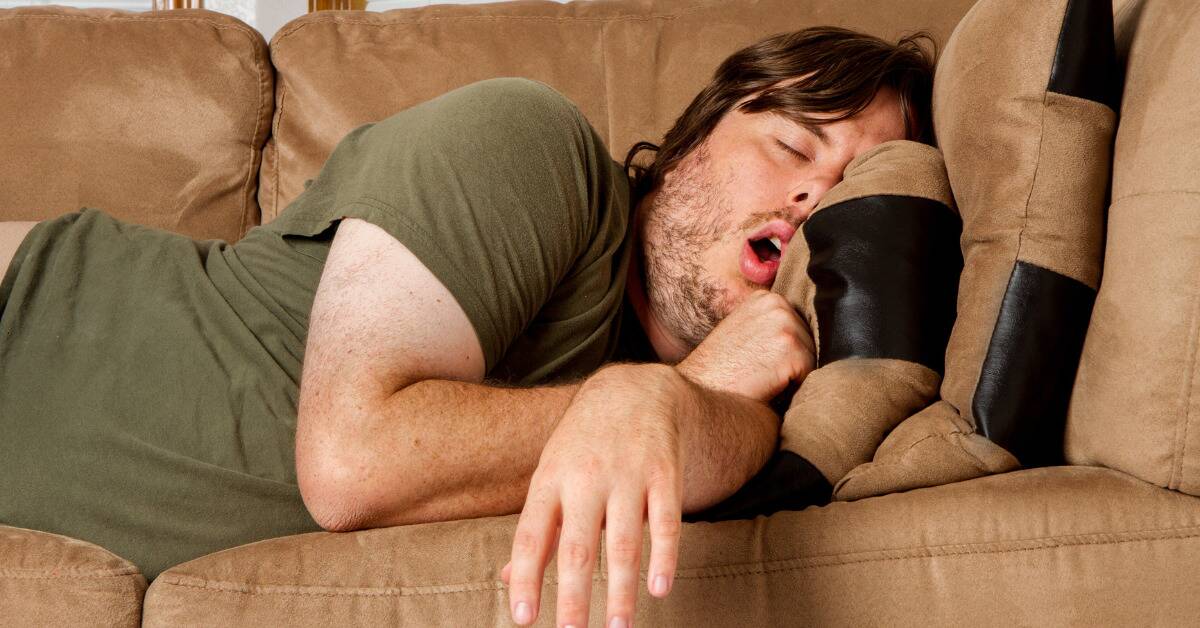 A man sleeping on the couch, mouth open in a snore.