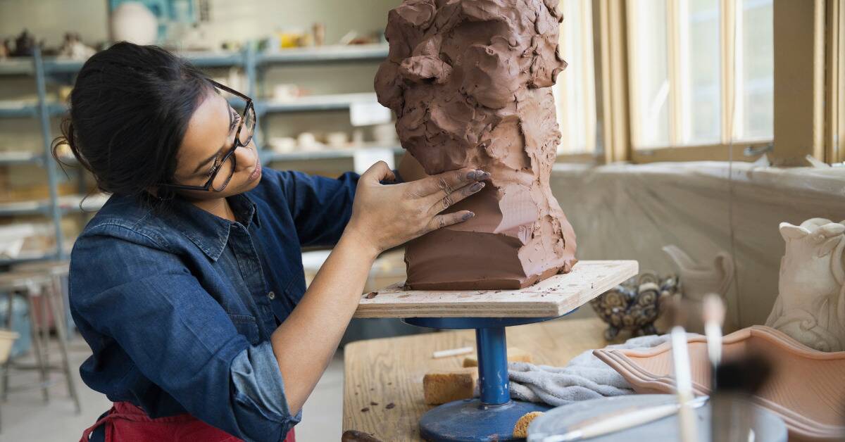 A woman working on a clay sculpture.