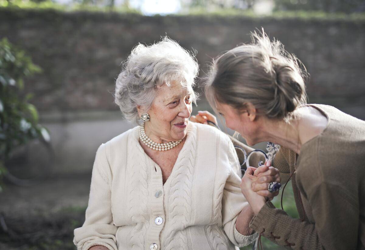 An older woman speaking to and smiling with a younger woman, the two are holding hands.