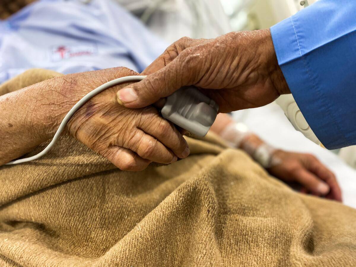 Two older people holding hands, one with a heart rate monitor on their finger.