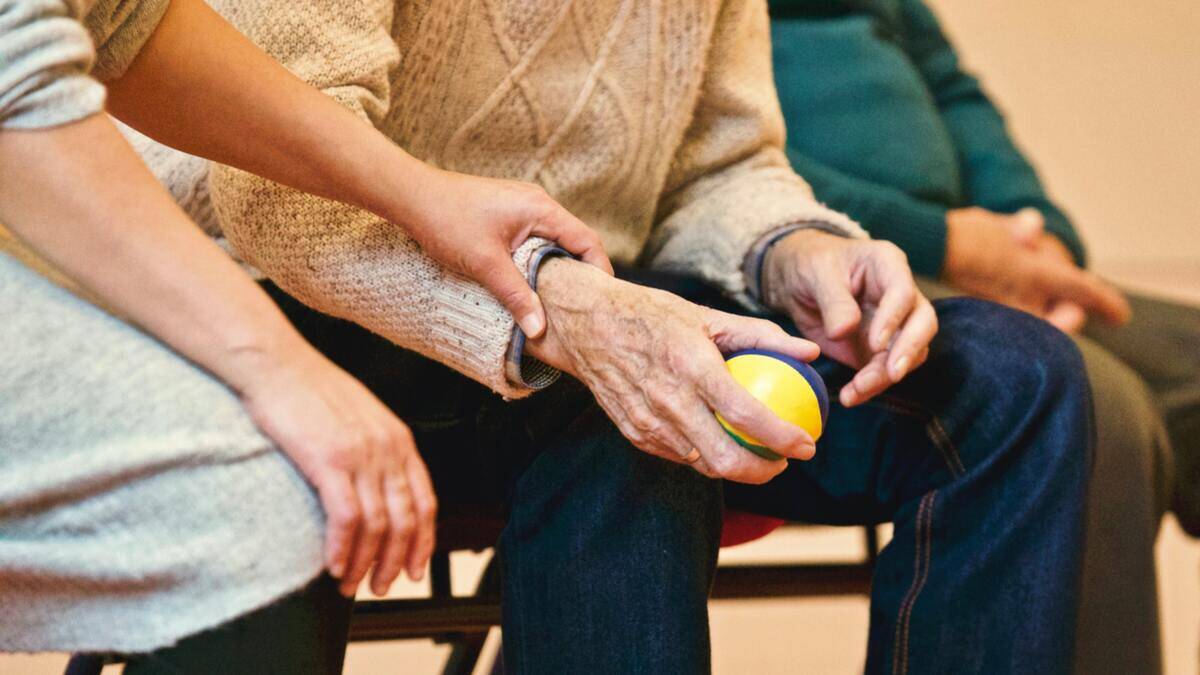 A younger woman's hand bracing an older person's wrist while the older person holds a ball, presumably doing some sort of hand exercise.