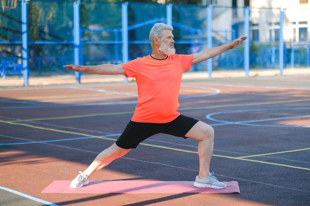 An older man doing a lunge stretch in a public park.