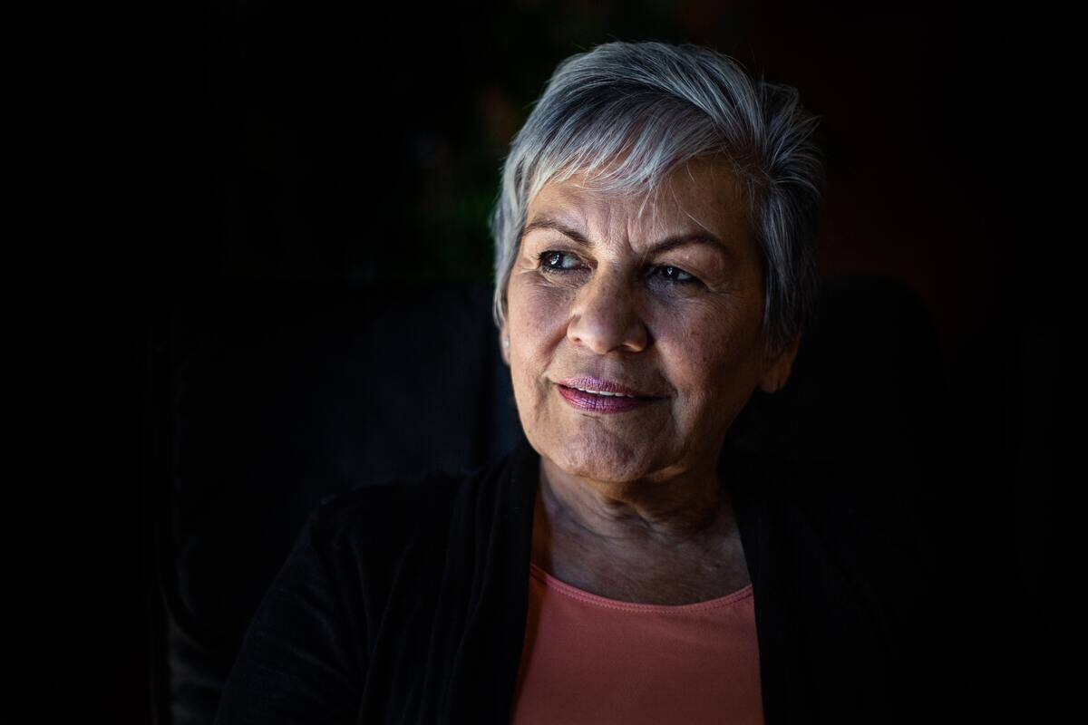 A portrait of an older woman against a black background with heavy shadows.