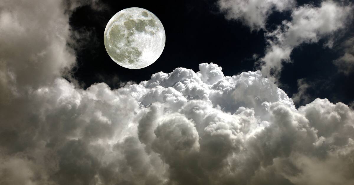 The moon in a dark sky full of fluffy white clouds.