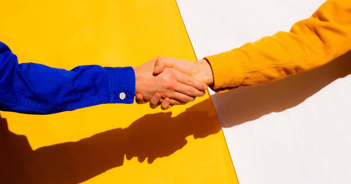 Two people in bright colored shirts shaking hands in front of an equally bright background.