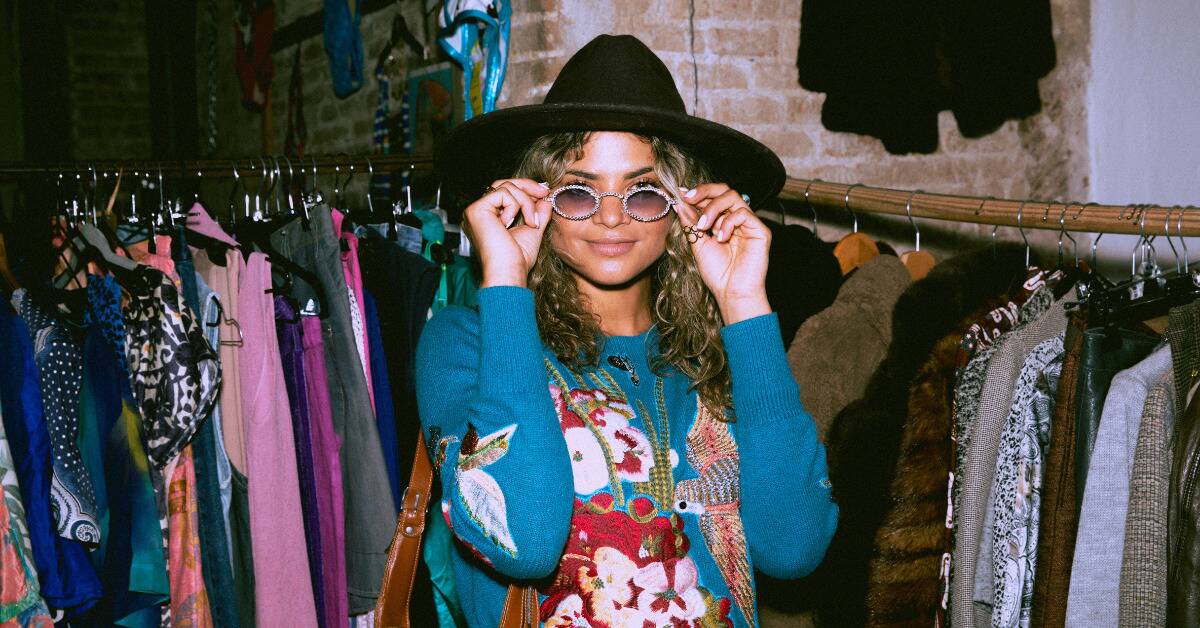 A woman in a thrift store with an array of quirky, unique fashion on.
