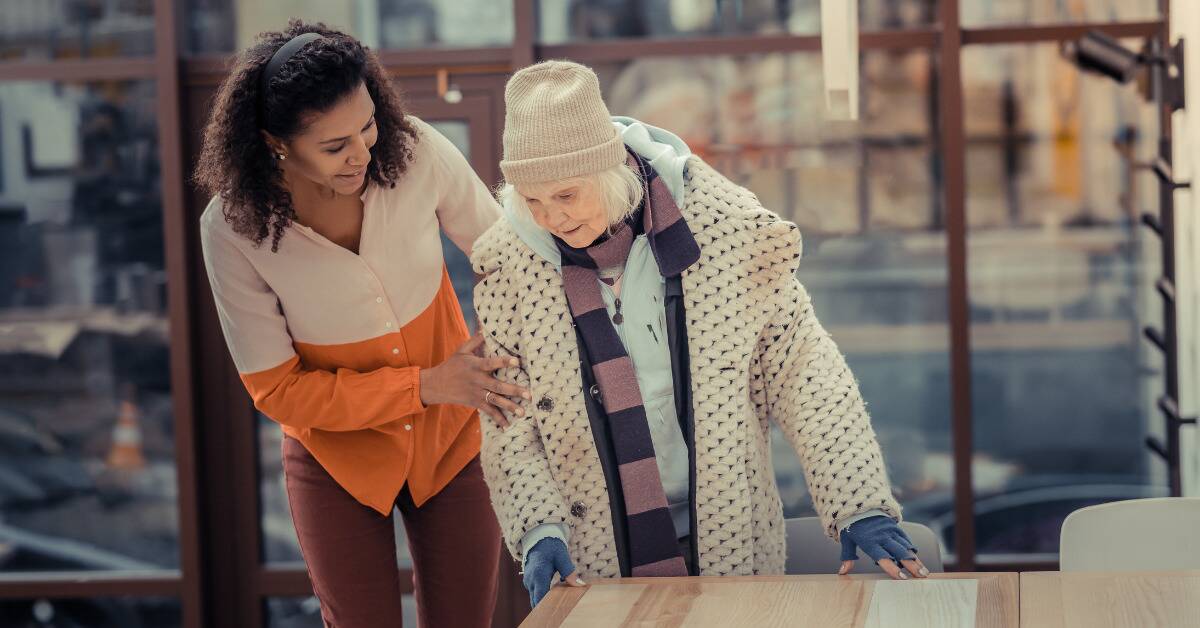 A woman helping a senior woman up from a table.