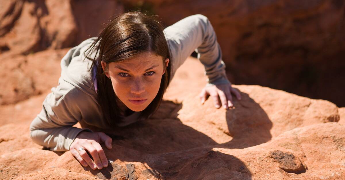 A woman looking at the camera intensely as she climbs a rock wall.