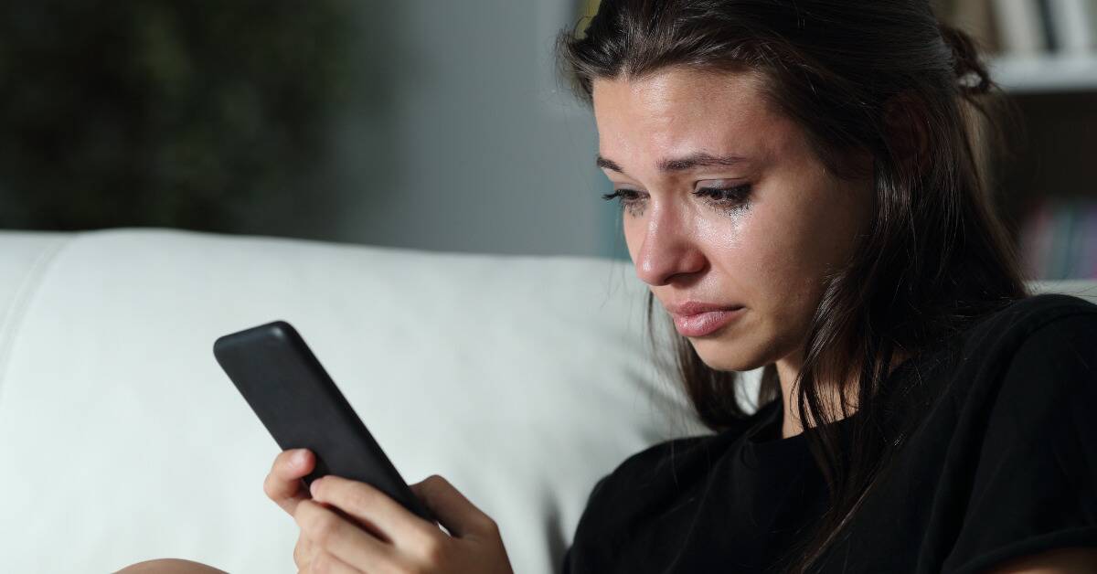A woman crying as she reads her phone.