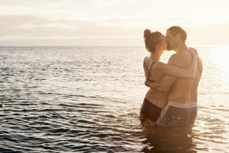 A couple kissing as they both stand in a body of water.