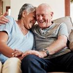 An older couple smiling as they embrace on the couch.