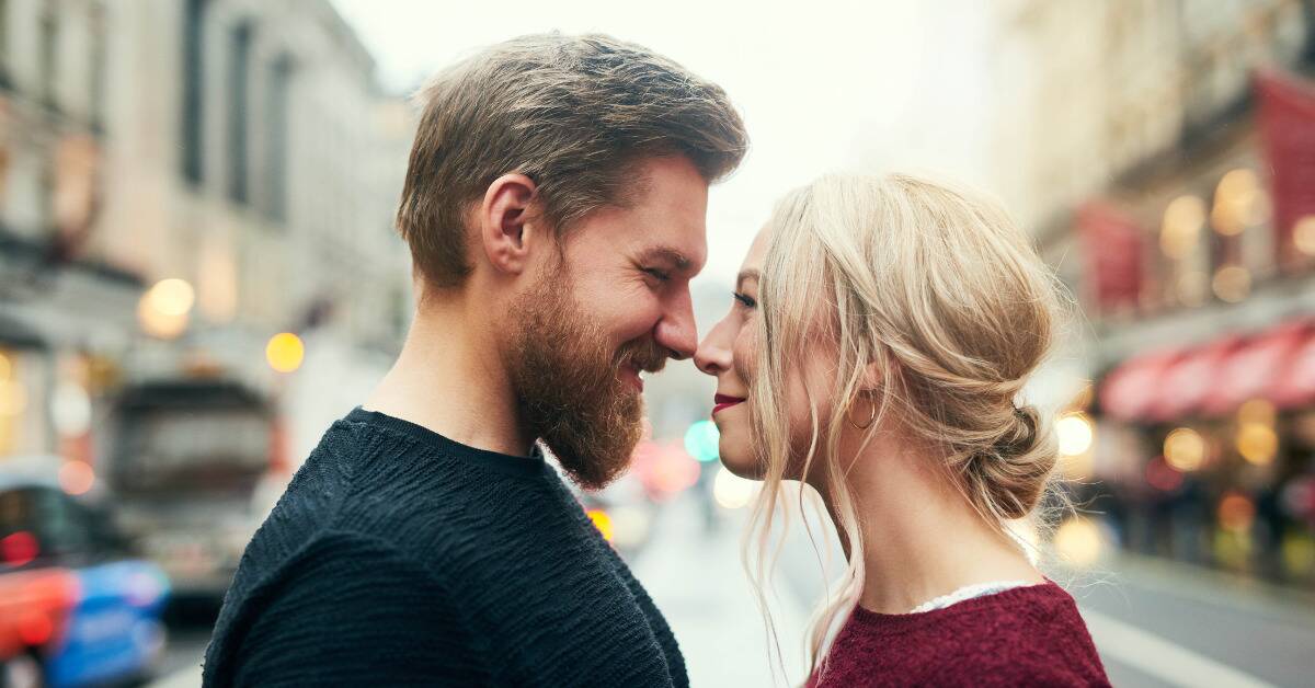 A couple standing nose-to-nose, smiling, in the middle of a street.