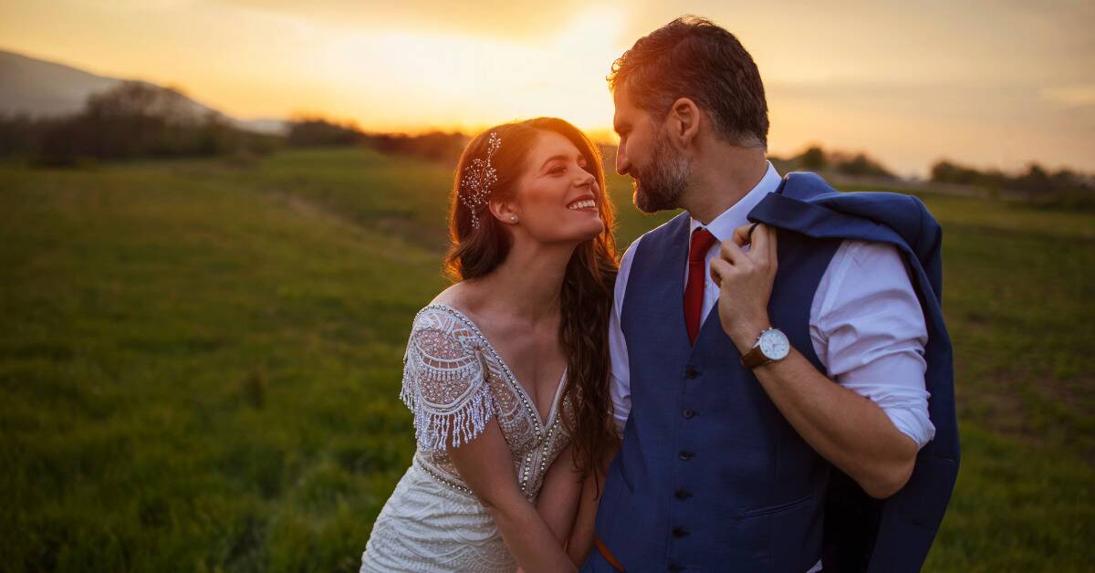 A couple on their wedding day looking at each other lovingly in front of the sunset.