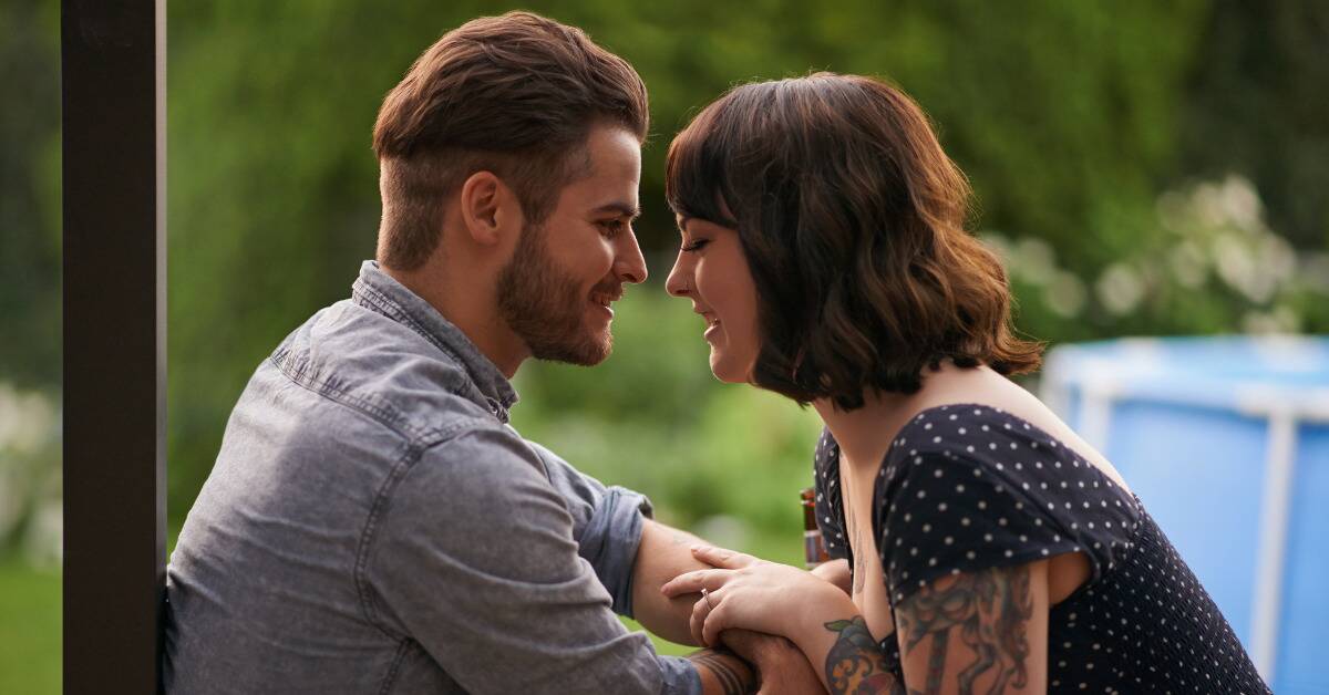 A couple sitting and facing one another, the woman's eyes closed in laughter while the man looks at her.