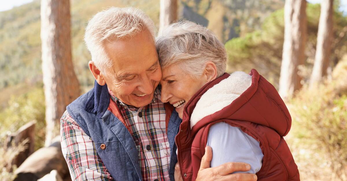 An older couple smiling as they embrace each other.