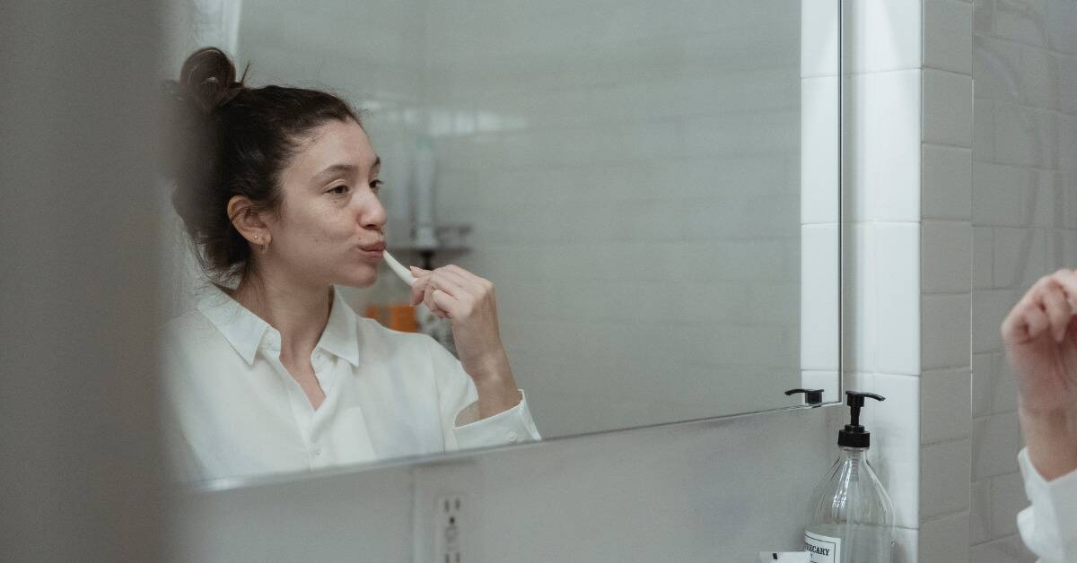 A woman brushing her teeth while looking in the mirror.
