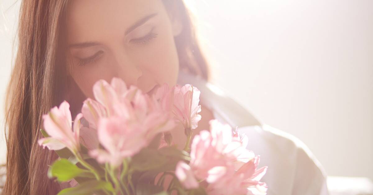 A woman leaning in to smell a bouquet of flowers.