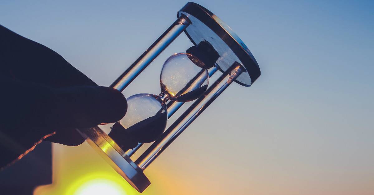 An hourglass held on an angle in front of a sunset.