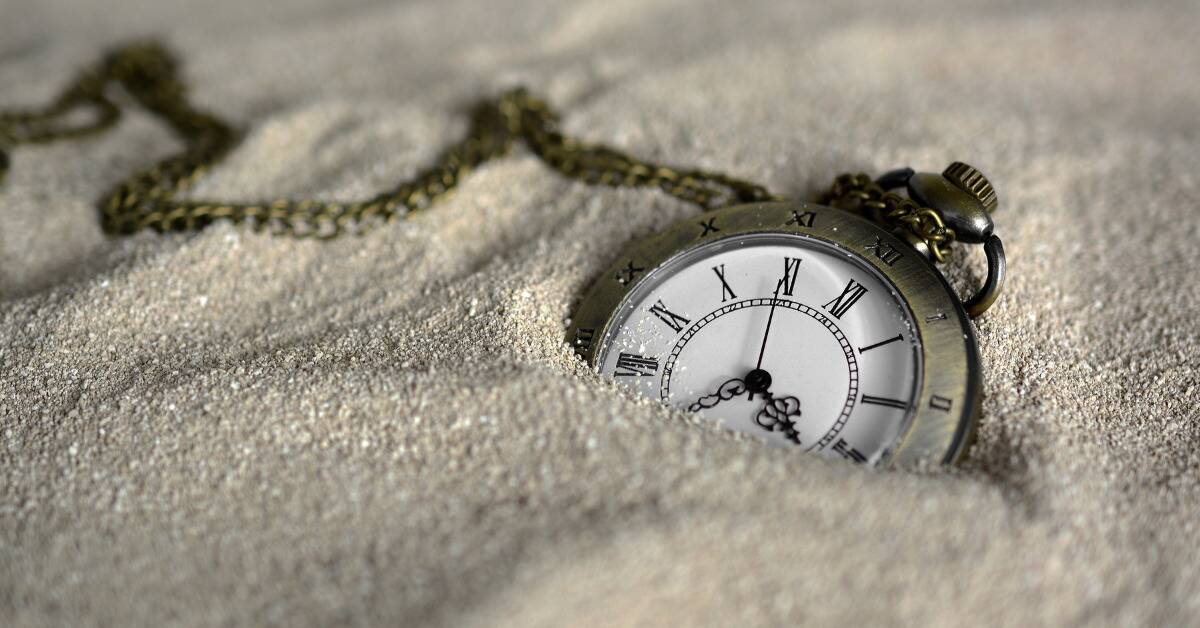 A stopwatch half-covered by sand.