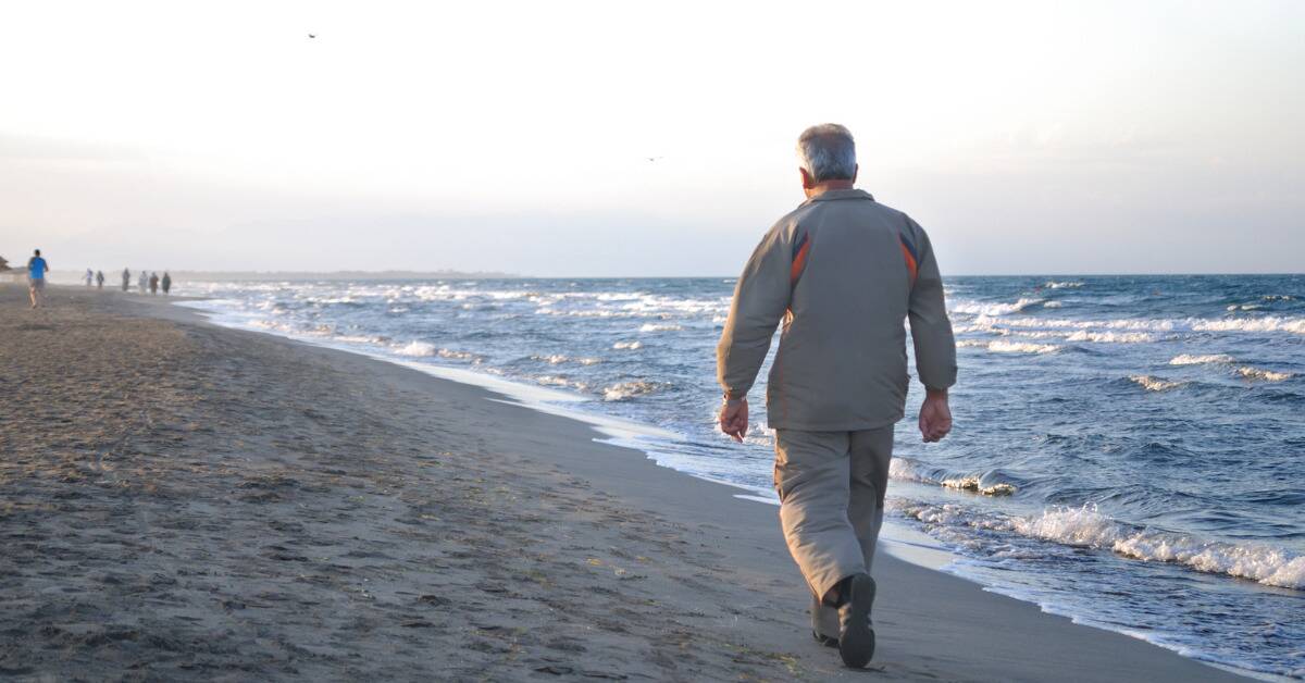 An older man walking alongside the shore at the beach.