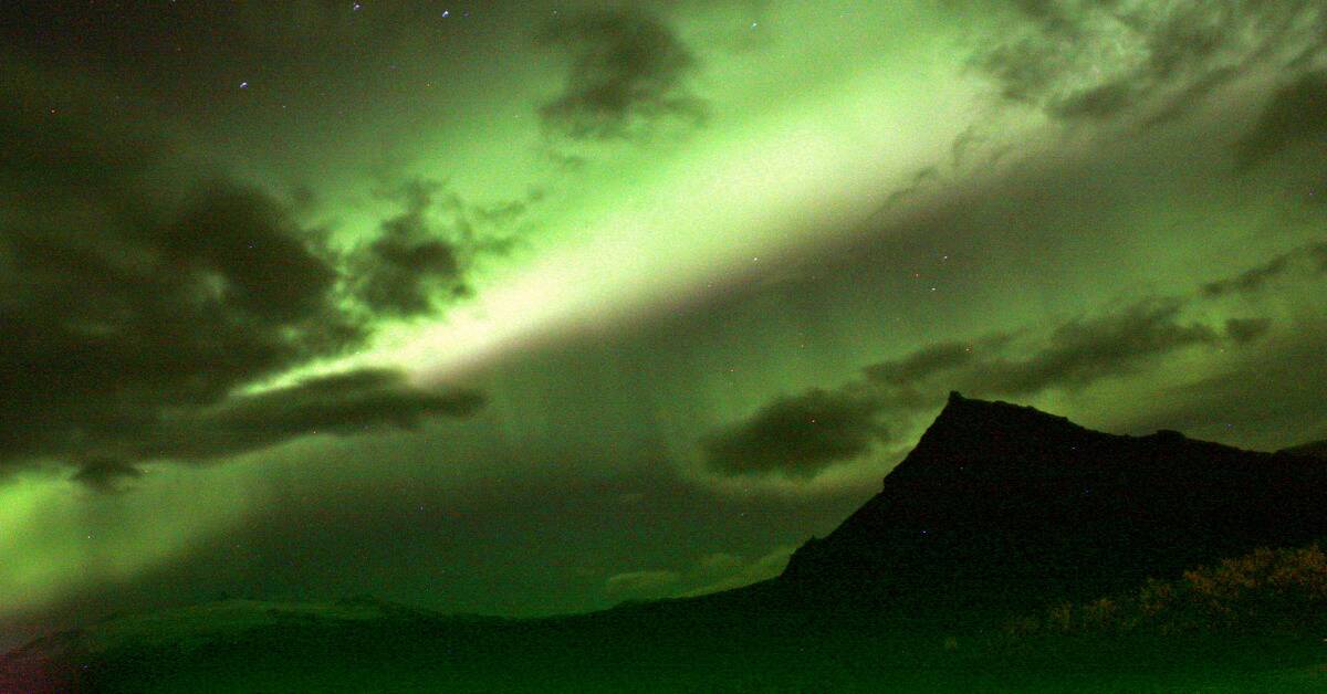 A green-tinted landscape shot of a mountain with the aurora borealis above it.