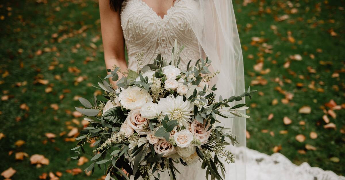 A bride holding a large bouquet in front of her dress.