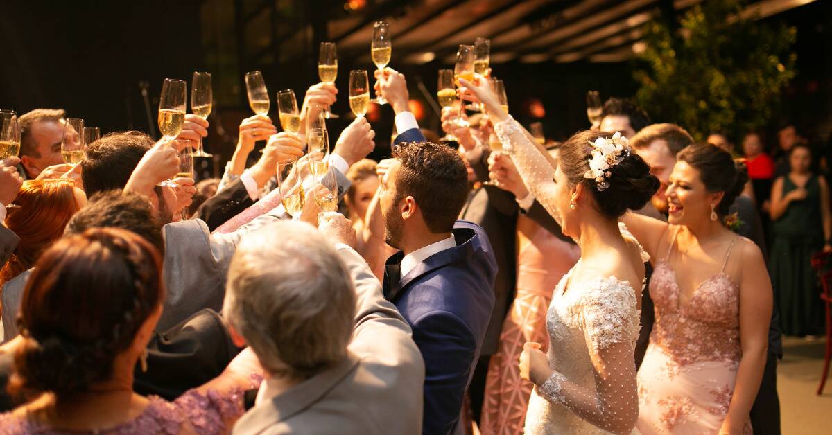A crowd at a wedding all gathered together, cheersing champagne glasses.