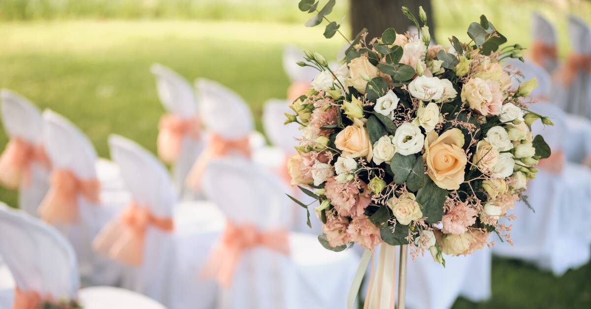 A flower stand along a wedding aisle, the seats in the background.