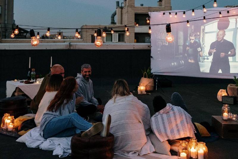 A group of friends hanging out on a rooftop watching a movie on a projector.