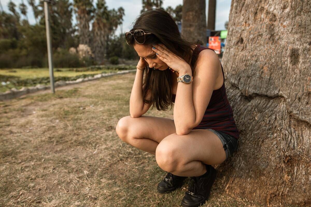 A woman crouched down next to a tree, looking stressed.