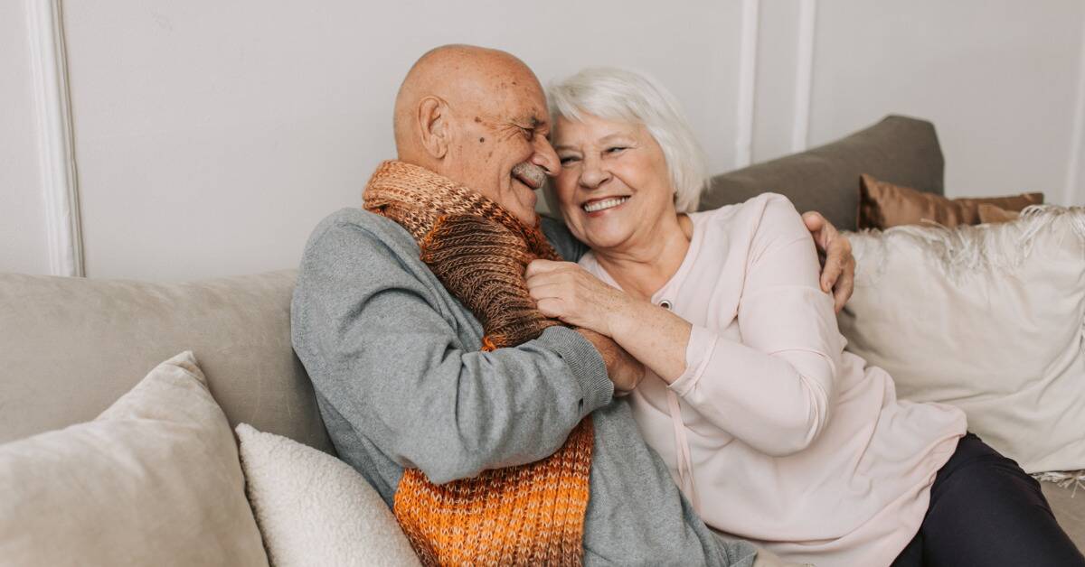 An older couple embracing as they sit on a couch.