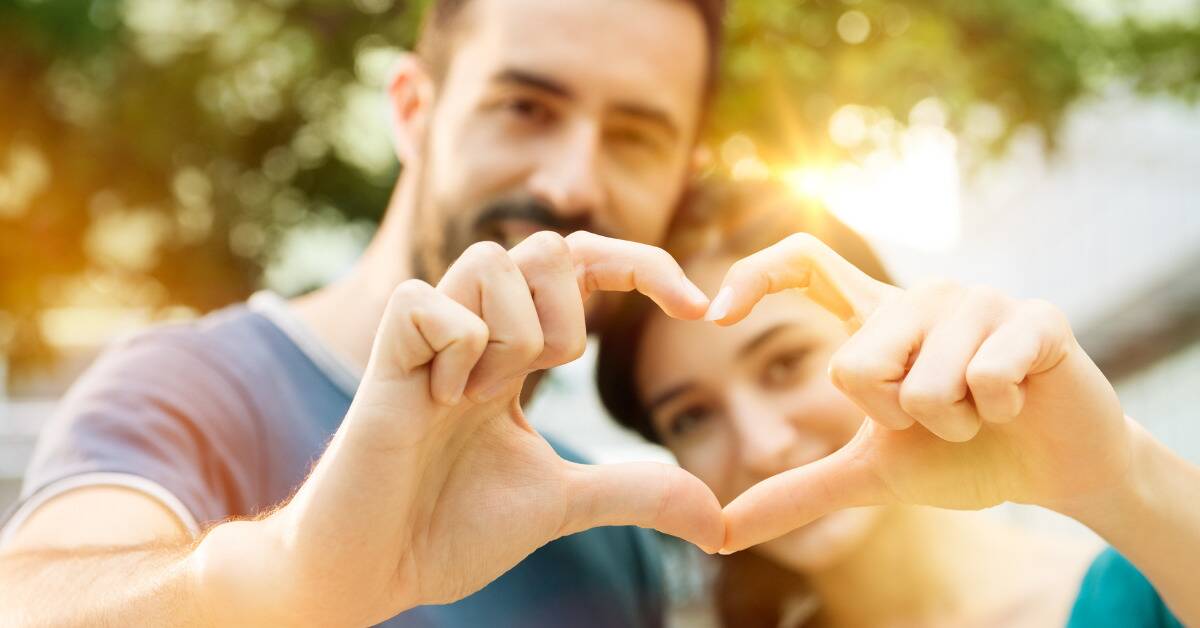 A couple making a heart with their fingers, held out in front of them.