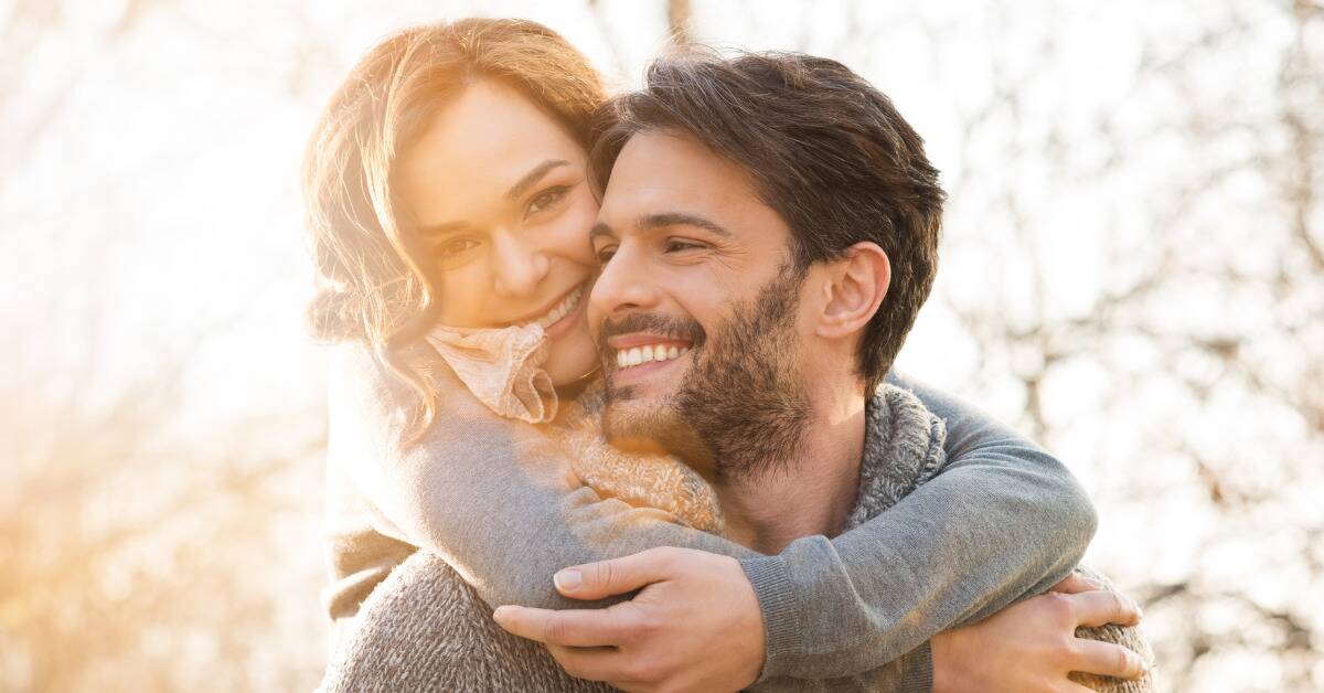 A woman hugging her boyfriend around the neck from behind.