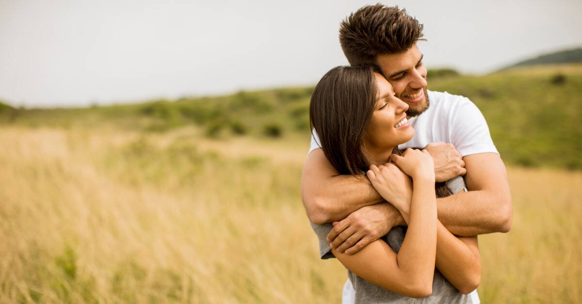 A man hugging his girlfriend from behind as they stand outside.