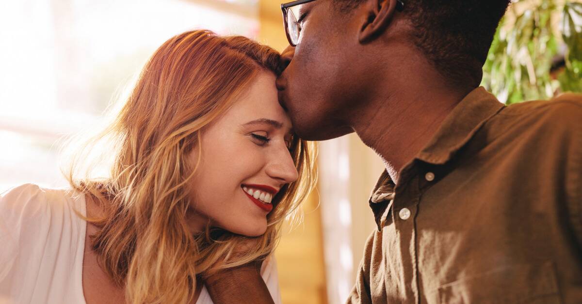 A close shot of a man kissing his girlfriend on the forehead.