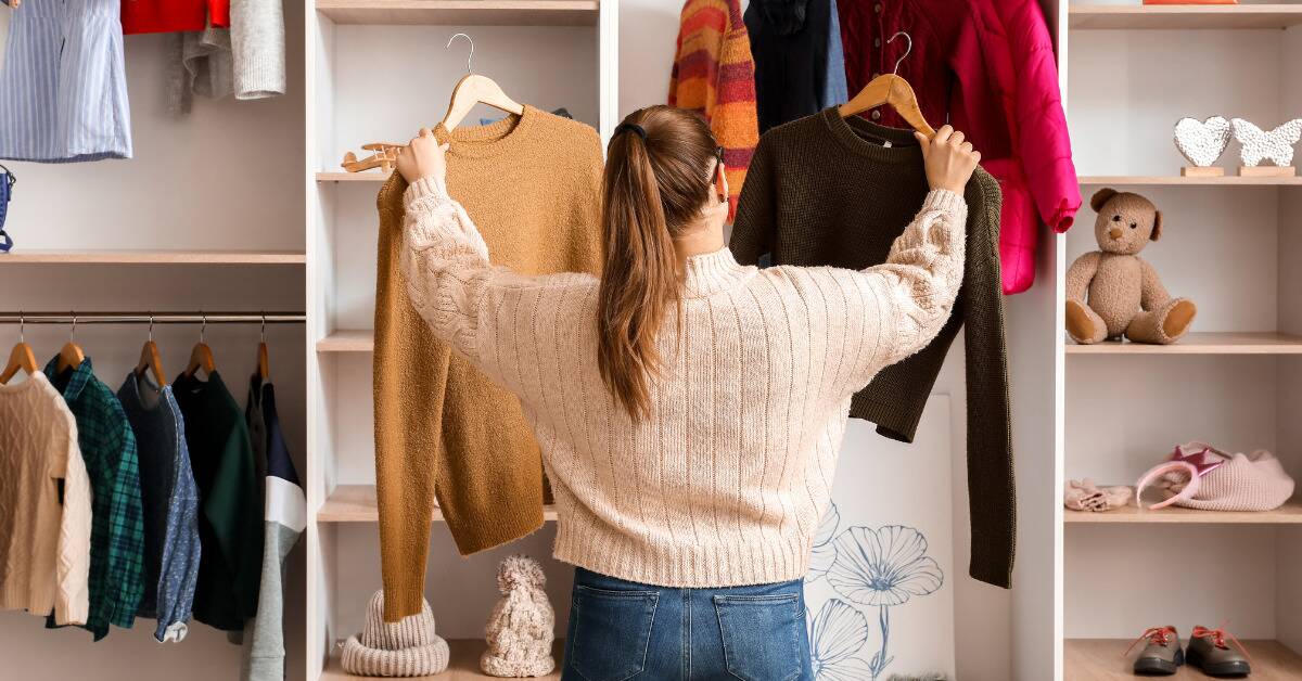A woman holding up two sweaters, trying to pick between the two.