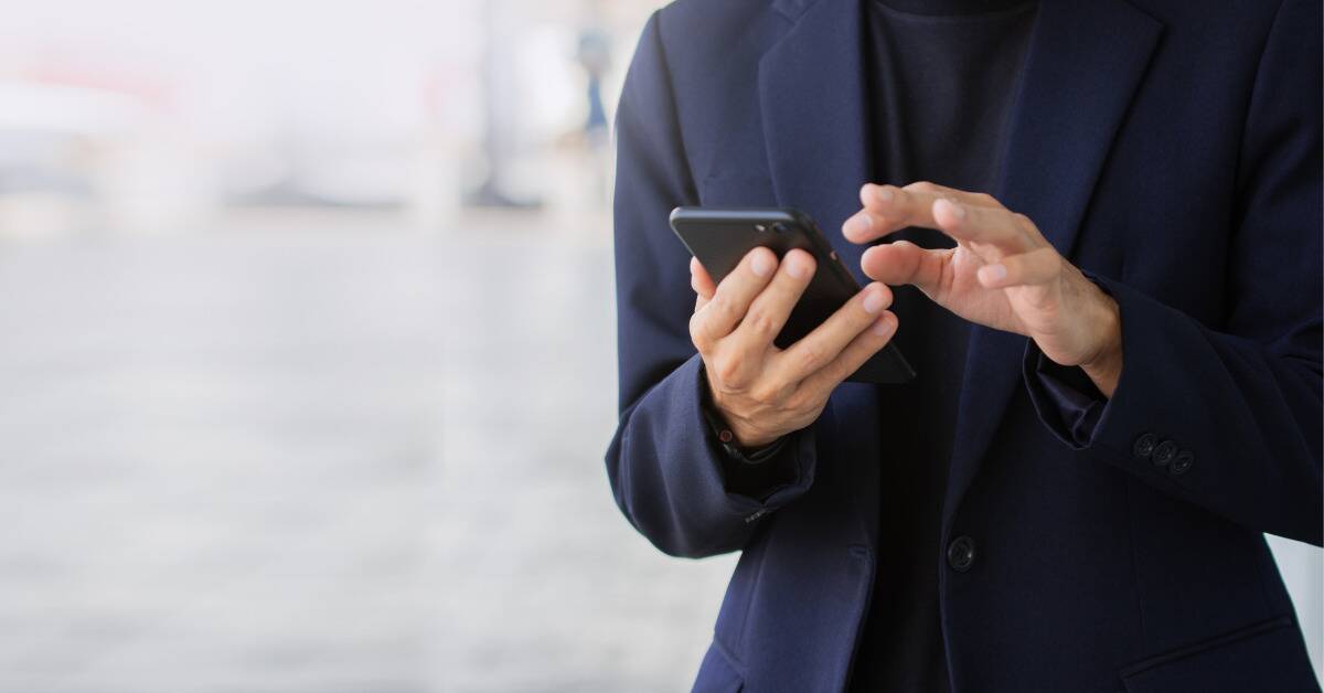 Someone in an all-black suit typing on a cell phone.