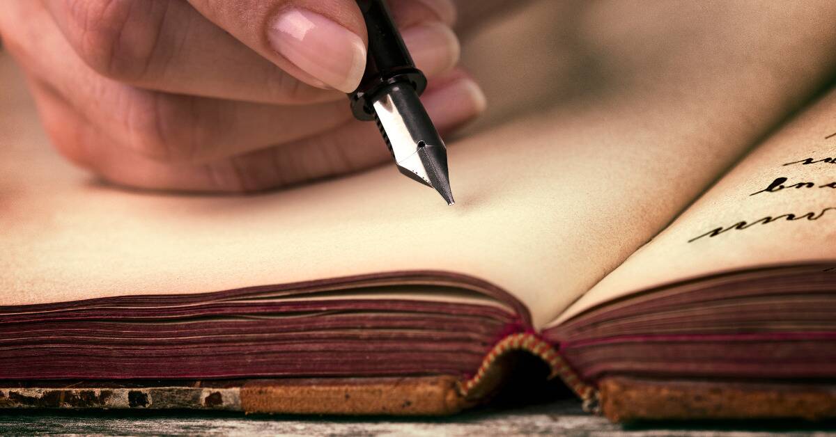 Someone holding a fountain pen, about to write in a journal.