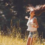 A woman laughing and tossing her hair as she stands in a sunny field.