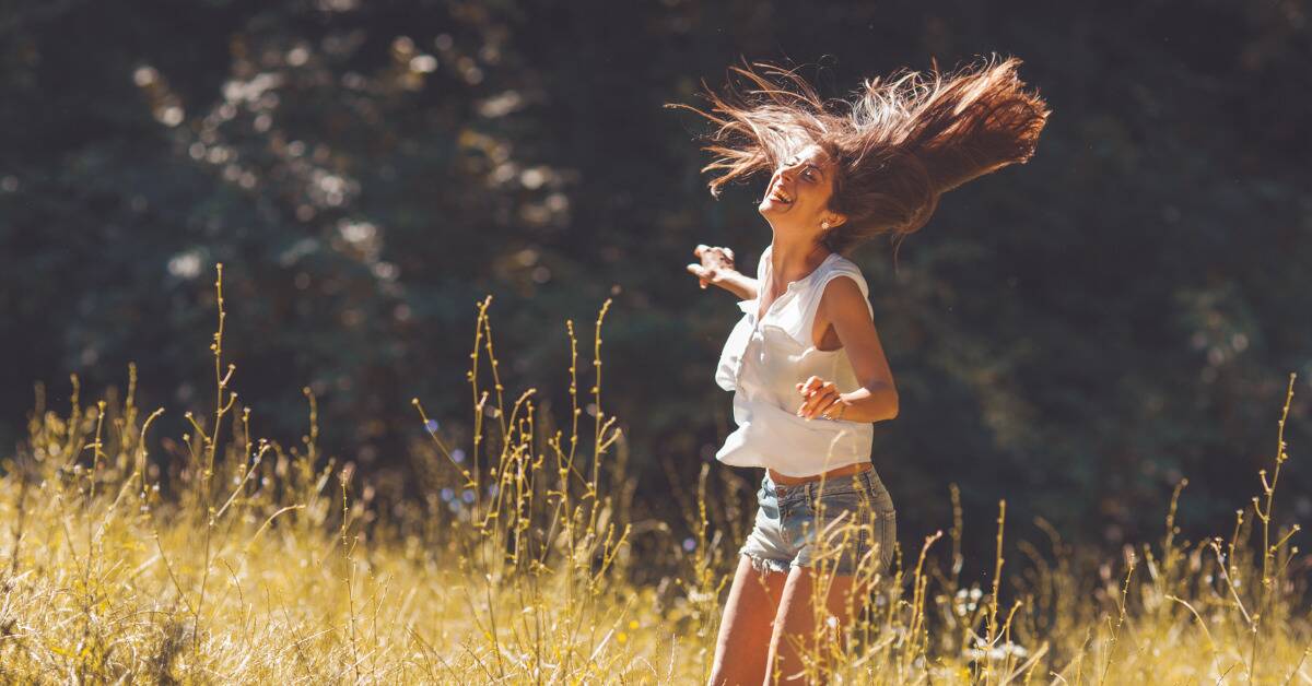 A woman laughing and tossing her hair as she stands in a sunny field.