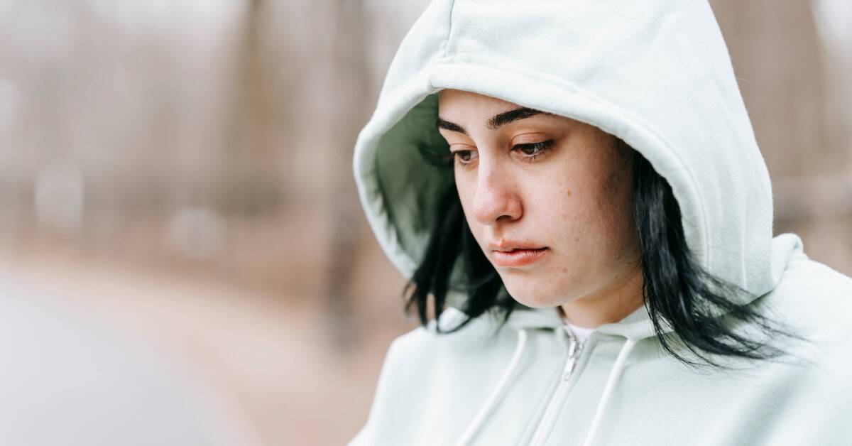 A woman with a hoodie on looking sad as she walks outside.