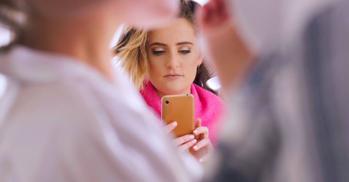 Two people in the foreground, blurred out, and a woman visible between them with her phone out.