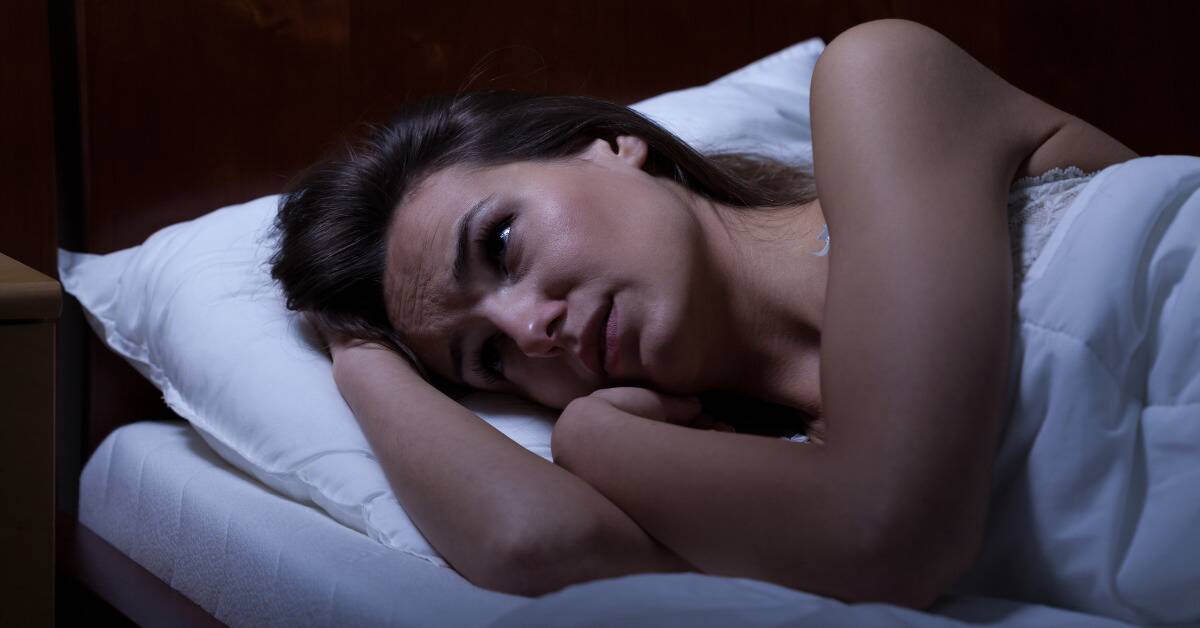 A woman laying in bed, looking stressed.
