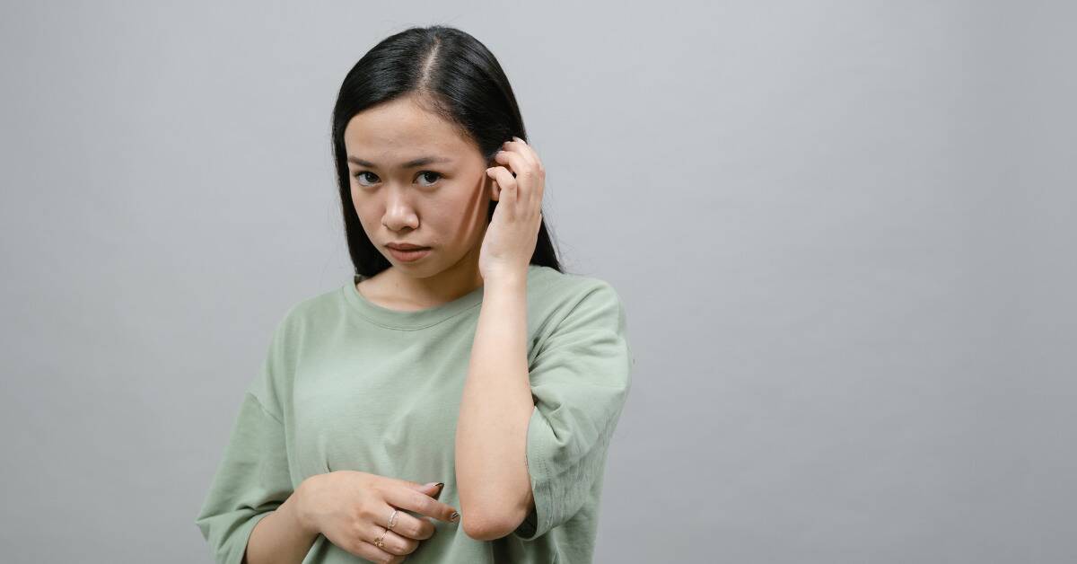 A woman looking very shy, tucking her hair behind her ear as she looks at the camera nervously.