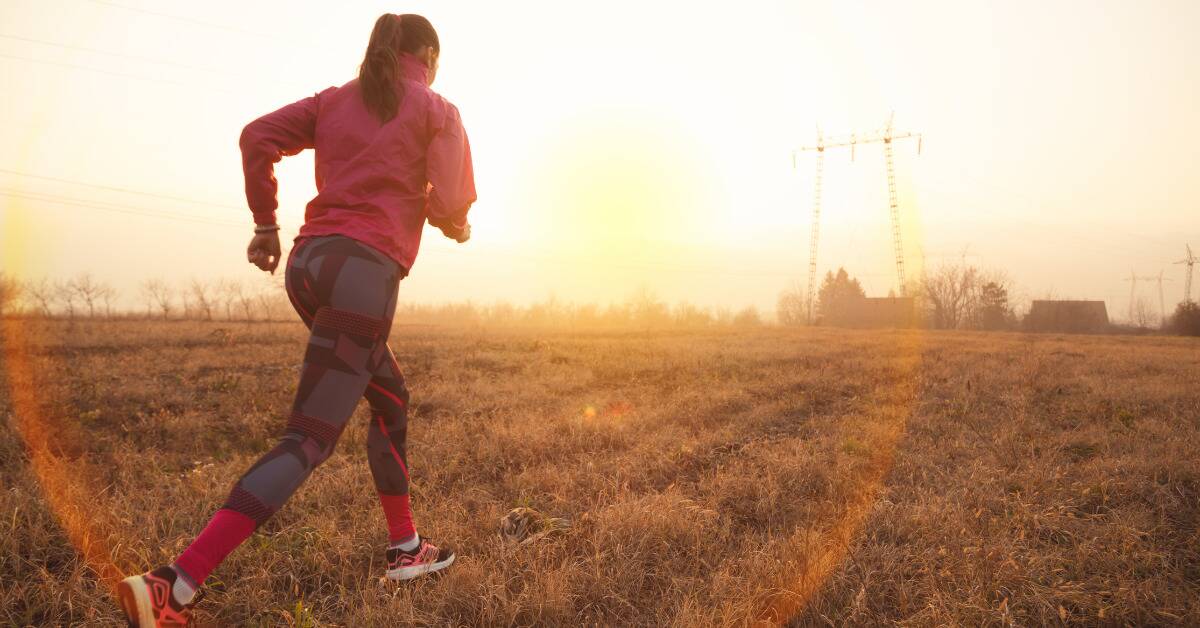 A woman in sportwear running through a field at sunrise.