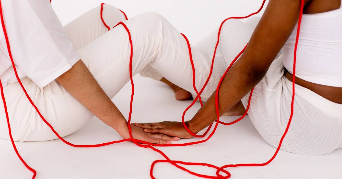 Two people sitting next to each other, red string connecting them both.
