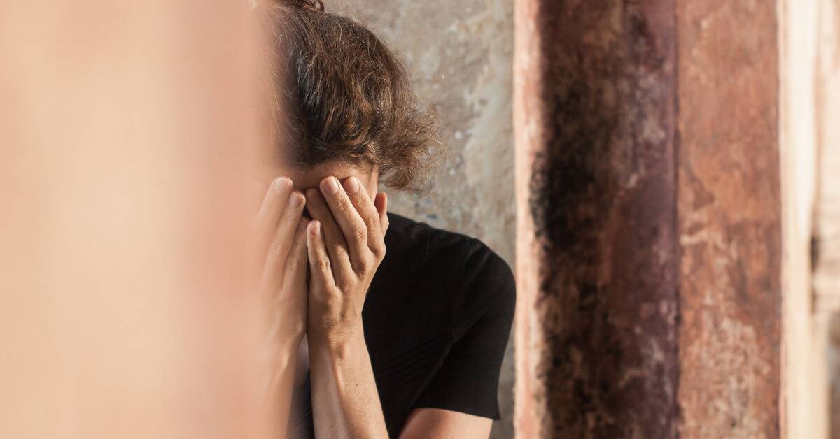 A woman looking stressed behind a wall, face covered by her hands.