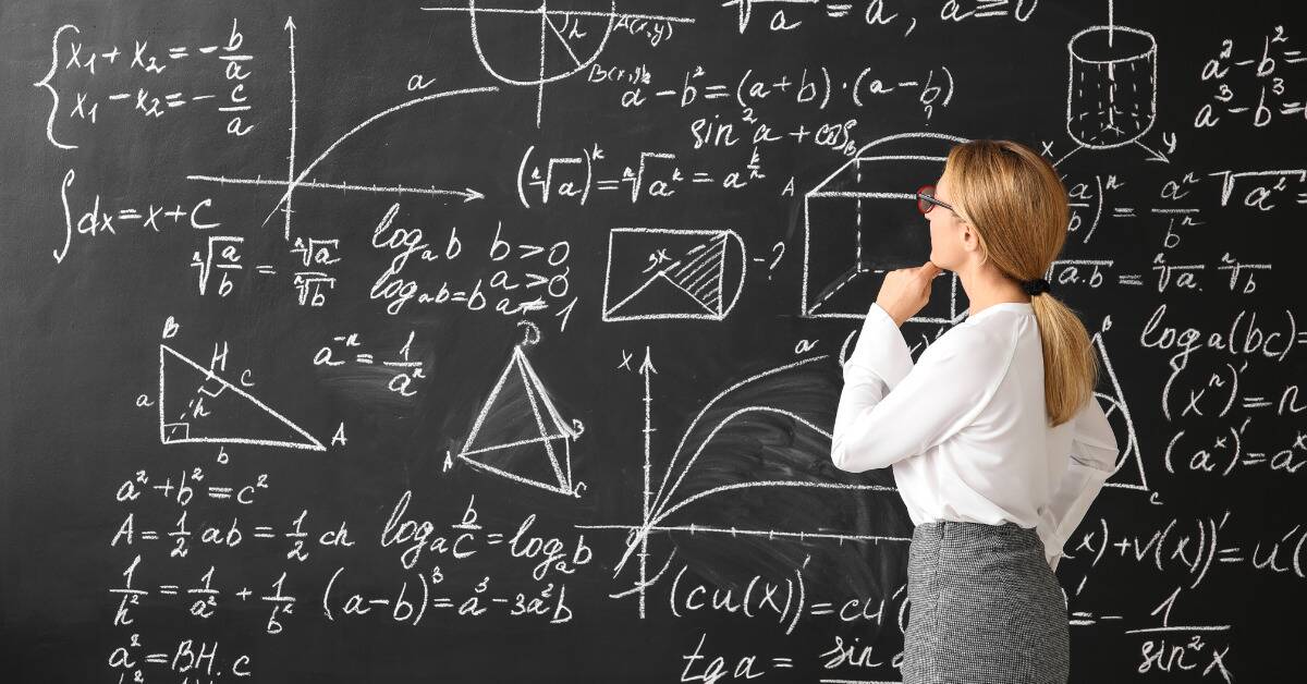 A math teacher looking at large equations on a blackboard.